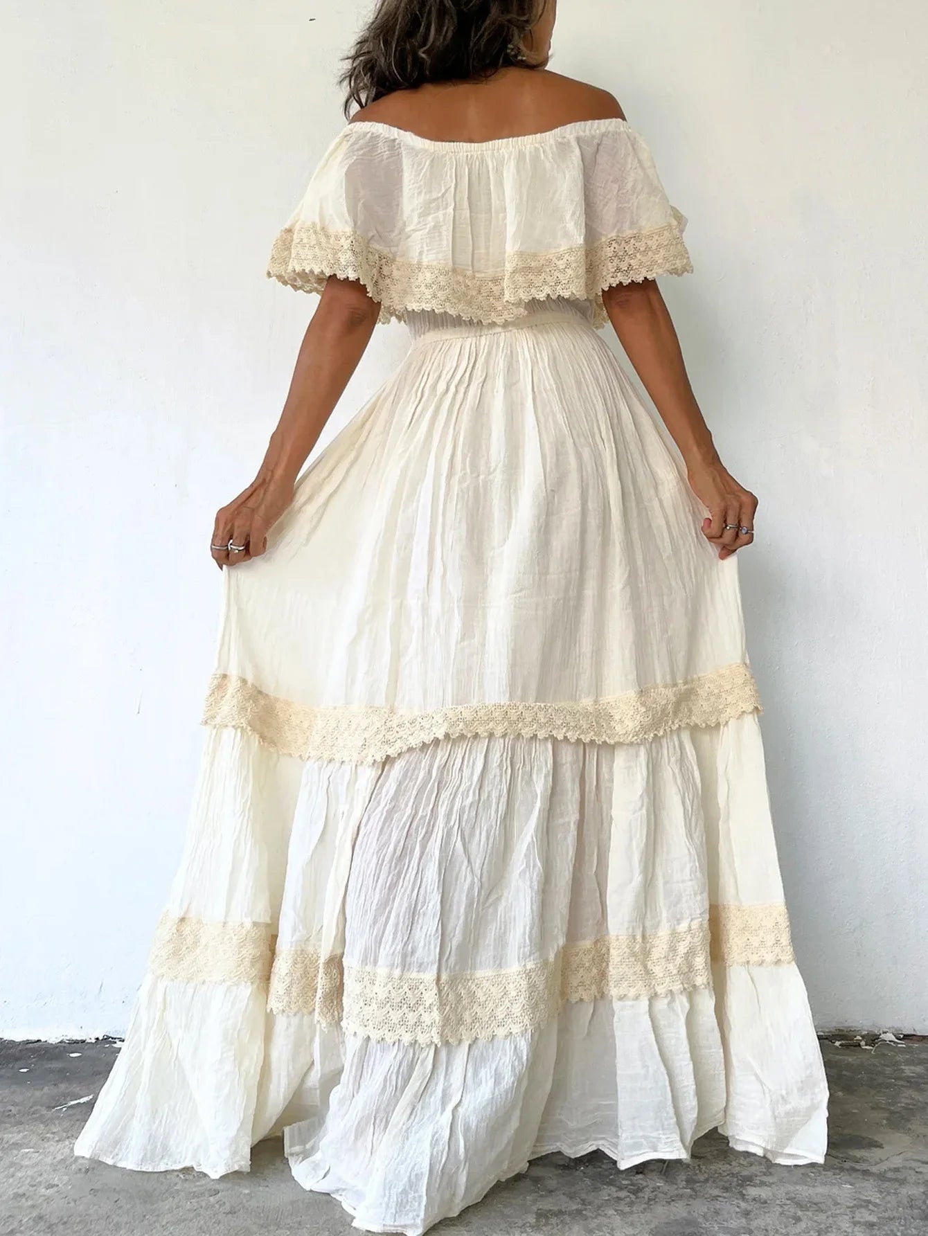 Woman wearing a white off-shoulder dress with lace details against a plain background