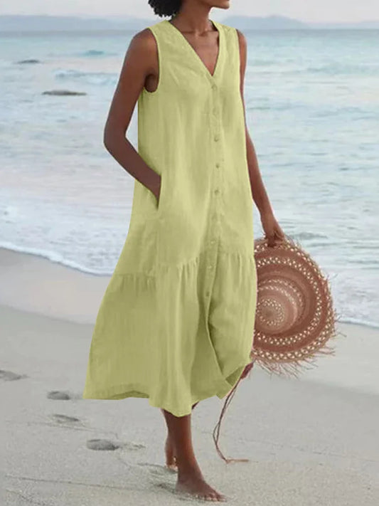 Woman in a light green dress standing on a beach with a straw hat.