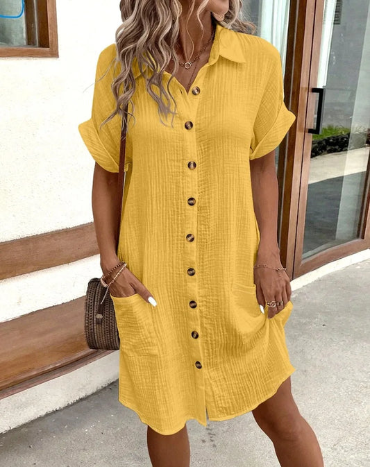 Woman wearing a yellow button-up dress standing outdoors.