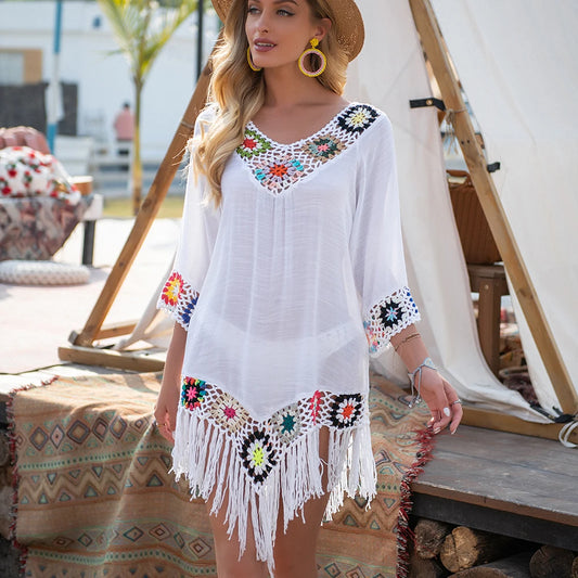 Woman wearing a white dress with colorful embroidery and fringes in a casual outdoor setting.