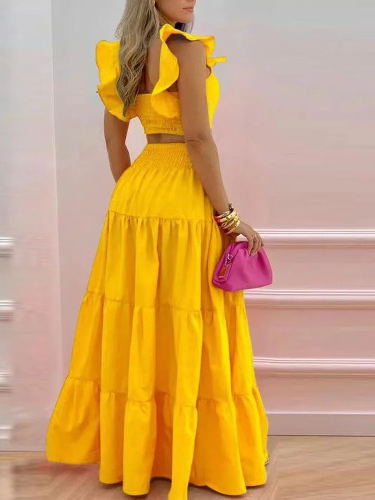Woman wearing a yellow dress with ruffled sleeves and a pink handbag against a light background